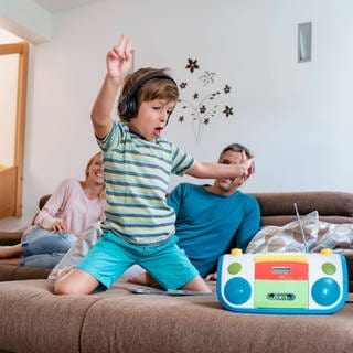 Junge hört mit Kopfhörern Musik während seine Eltern im Hintergrund auf dem Sofa sitzen