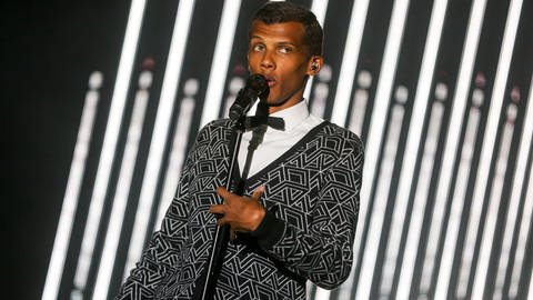 Stromae tritt beim 2015 Coachella Music and Arts Festival in Indio, California auf, am 19. April 2015: Ein schmaler dunkelhäutiger Mann mit kurzen Haaren sing tin ein Mikrofon er trägt geomatrisch gemusterte Kleidung in Schwarz-weiß.