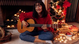 Young woman playing guitar while sitting at home during Christmas