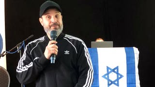 Ben Salomo, in Israel geborener Rapper und Referent zum Thema Antisemitismus, spricht vor einer israelischen Flagge bei einem Vortrag vor Schülerinnen und Schülern. 