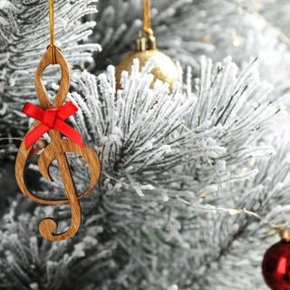 Ein Weihnachtsanhänger der eine Note darstellt hängt an einem weißen Baum 