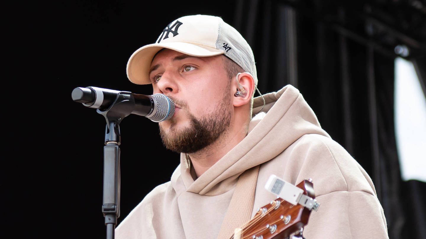 Der Musiker Luca Noel steht bei einem Konzert auf dem Ehrenhof des Barockschlosses Mannheim mit seiner Gitarre auf der Bühne (2023).