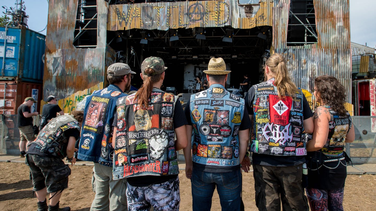 Einige Metalheads stehen auf dem Wacken Open Air in ihren Kutten vor einer Bühne