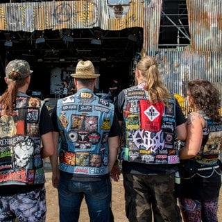 Einige Metalheads stehen auf dem Wacken Open Air in ihren Kutten vor einer Bühne 