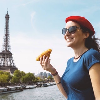 Frau mit Croissant steht vor dem Eiffelturm