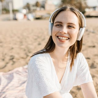 Glückliche junge Frau am Strand hört Musik.