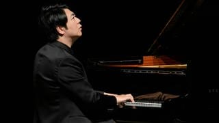 Pianist Lang Lang am Flügel, mit dem Rücken zum Publikum. Er blickt verträumt in die Ferne.