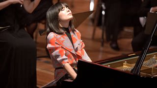 Die Pianistin Alice Sara Ott: Frau mit geschlossenen Augen und dunklen, glatten Haaren am Flügel während eines Konzerts