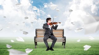 Violine spielender Mann auf Bank, umgeben von Papierfliegern