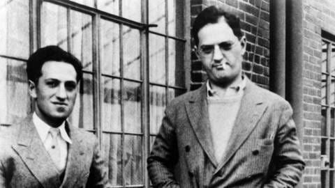 Schwarz-weiß-Fotografie der Brüder George und Ira Gershwin in Anzügen vor einem Fenster. 