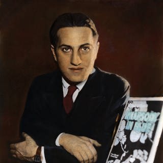 Kolorierte Porträtaufnahme von George Gershwin mit Anzug und zurückpomadierten Haaren.