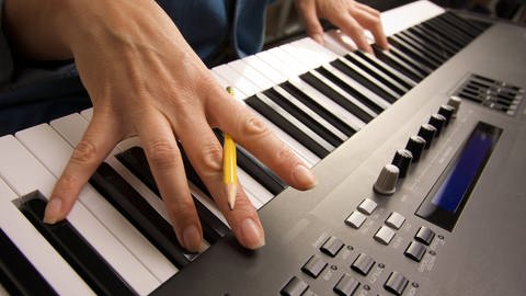 Frauenhände beim Klavierspielen auf der Klaviatur. Zwischen den gespreizten Händen Fingern sie einen Bleistift.