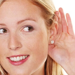 Eine junge Frau hält sich beim zuhören die Hand hinter das Ohr