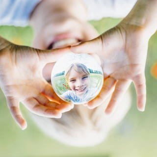 Ein Kind spiegelt sich in einer Kugel aus Glas