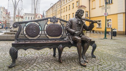 Bronze-Statue von Georg Philipp Telemann in Żary (Polen): Der Komponist sitzt Geige spielend auf der linken Seite einer barocken Rattan-Bank.