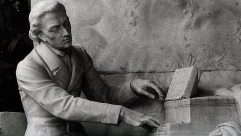 Chopin-Denkmal im Parc Monceau in Paris: Chopin sitzt am Flügel und blickt hinab zu einer weiblichen Figur in trauernder Pose.