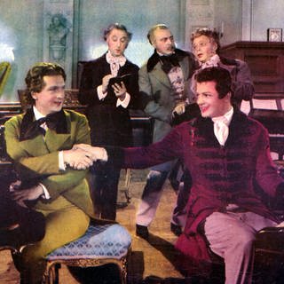 Farb-Werbefoto für den Film "Polonaise" ("A Song to Remember", USA 1945). Franz Liszt (Stephen Bekassy) und Frédéric Chopin (Cornel Wilde) sitzen Rücken an Rücken am Piano und reichen sich freundschaftlich die Hand.