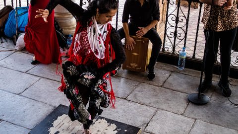 Flamenco-Tänzerin in Sevilla tanzt auf einem Brett, im Hintergrund Zuschauer und ein Musiker an einer Cajón.