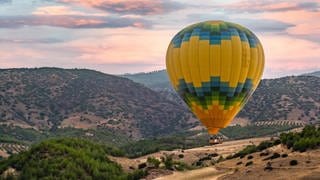 Ein Heissluftballon fliegt über eine weite Ebene. 