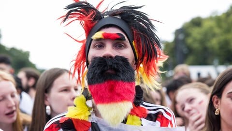 Fußball-Fan mit Franartikeln in den deutschen Nationalfarben: Perücke, künstliche Augenbrauen, Bart, Blumenkette und deutsches Nationaltrikot.