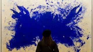 Eine Frau steht vor einem Gemälde des Künstlers Yves Klein