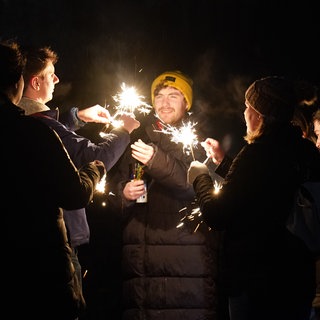 Junge Leute in Edinborough feiern Neujahr auf der Straße mit Wunderkerzen und Sekt