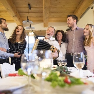 Älterer Mann spielt Akkordeon für eine glückliche Familie - Symbolfoto