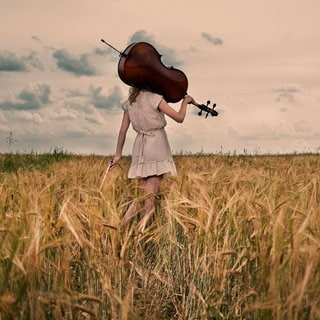 Ein Mädchen trägt in einem Weizenfeld ein Violoncello auf der Schulter