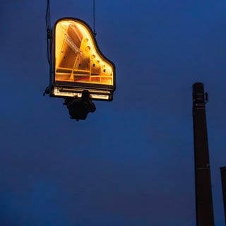 Projekt PIANO VERTICAL: Alain Roche spielt frühmorgens am Kran hängend in luftiger Höhe Klavier, Werksviertel-Mitte, München, Dezember 2023.