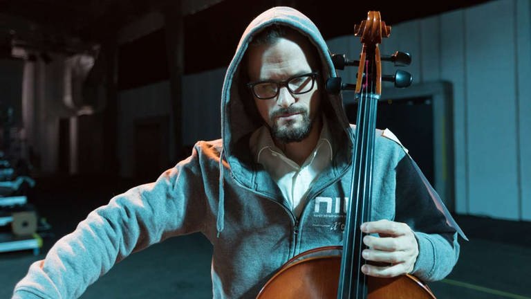 Mann mit Kapuze spielt sein Cello in der Probe fürs Konzert