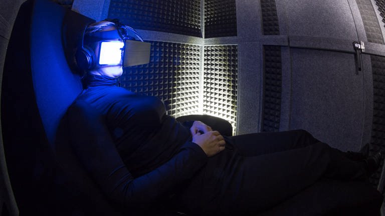 Eine Frau liegt mit einer Datenbrille und Kopfhörern in einer schallisolierten Tonne