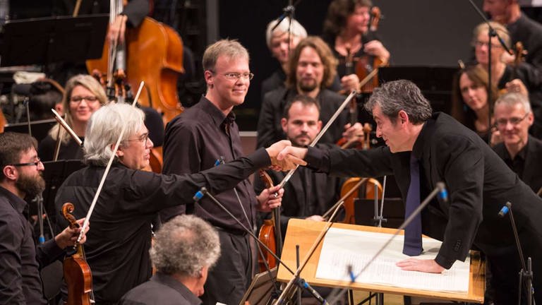 Dirigent gratuliert Cellisten nach der Uraufführung