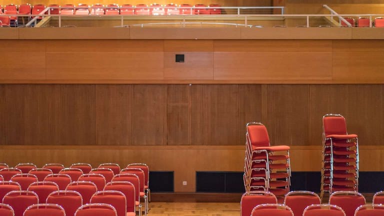 Leere Konzerthalle mit roten, zum Teil gestapelten Stühlen