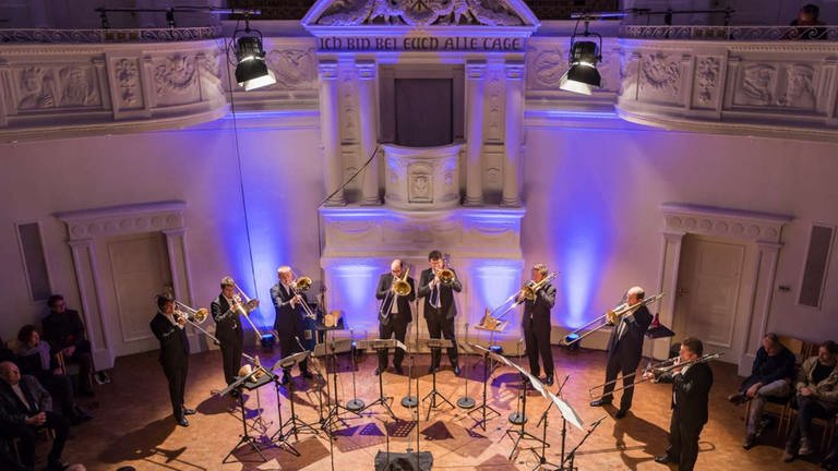 Acht Posaunenspieler der Trombone Unit Hannover stehen im Halbkreis und spielen das Stück von Georg Friedrich Haas