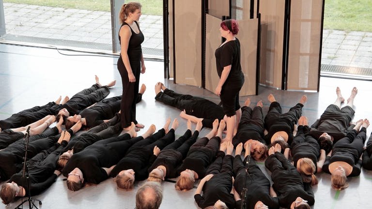 Viele schwarz gekleidete Schülerinnen liegen am Boden, zwei stehen sich gegenüber