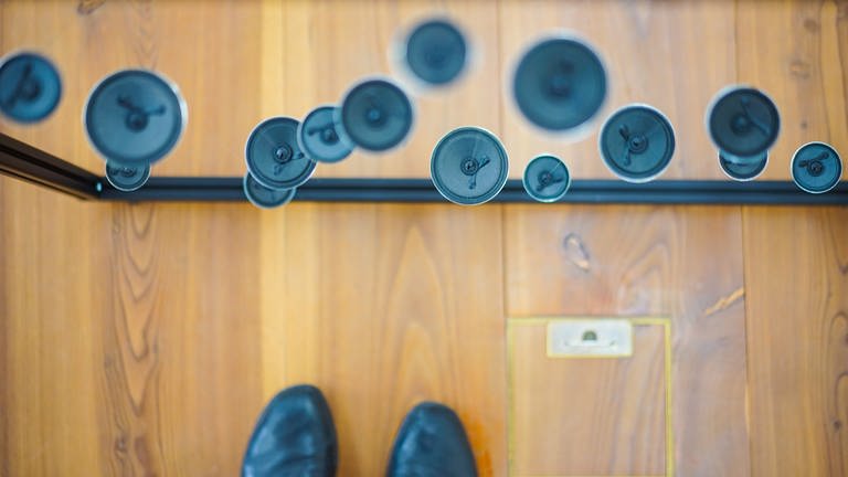 Donaueschinger Musiktage: Blick von oben auf schwebende Lautsprecher und schwarze Schuhe auf einem Holzboden