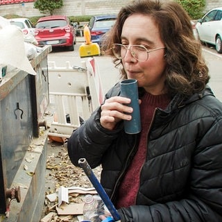 Kate Carr von Rubbish Music bläst in ein Rohrstück aus einem Müllcontainer