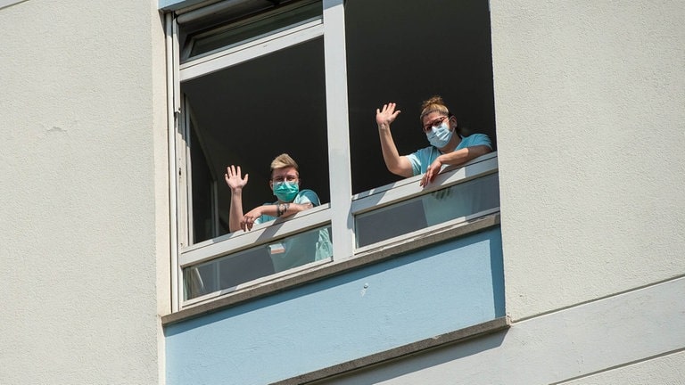 Pflegerinnen winken aus einem offenen Fenster heraus