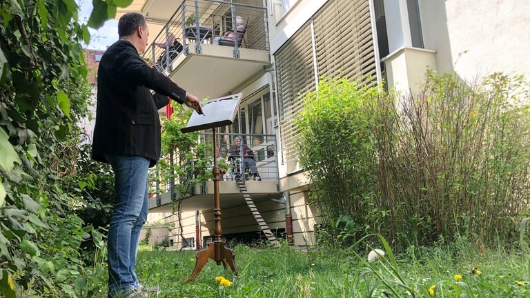 Musiker spielt im Freien vor Leuten, die auf Balkonen sitzen