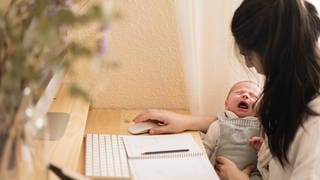 Eine Frau arbeitet am Computer und hat dabei ihr Baby auf dem Arm