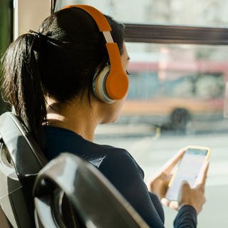 Eine Frau sitzt im Bus und hört mit Kopfhörern etwas über ihr Handy 