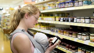 Mutter mit Säugling informiert sich beim Einkauf über die Inhaltsstoffe eine Produkts. Immer mehr Konsumenten wollen genau wissen, was in den Lebensmitteln steckt und erhöhen damit den Druck auf die Industrie.
