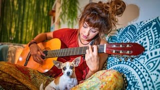 Eine junge Frau spielt Gitarre: Musikwissenschaftlerinnen und Hirnforscher versuchen in der Musik Merkmale zu identifizieren, die bei allen Menschen eines Kulturkreises oder sogar weltweit dieselben Gefühle auslösen