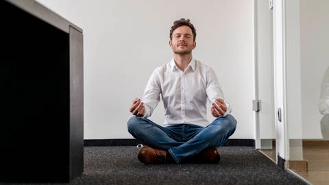 Mann meditiert im Büro. Achtsamkeitstrainings sollen die innere Einstellung zur Arbeit verändern, sodass Arbeitende weniger stressanfällig sind. 