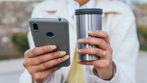 Frau mit Handy und Kaffeebecher in den Händen