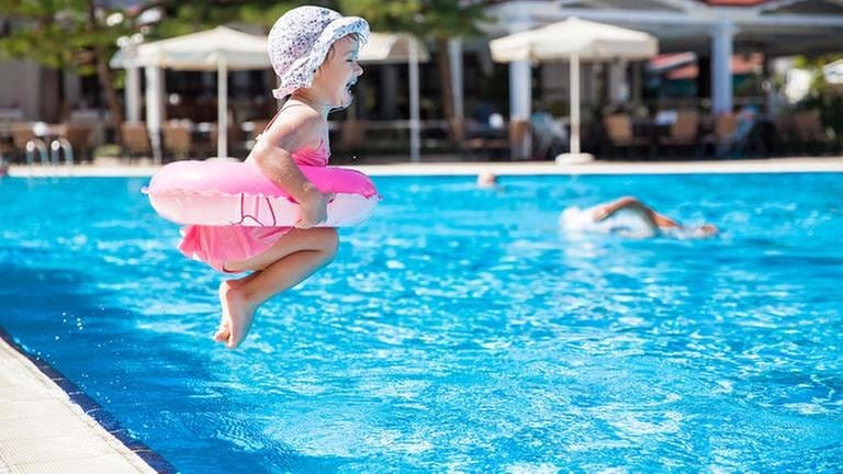 Ein kleines Mädchen mit Schwimmring hüpft in das Becken in einem Schwimmbad.