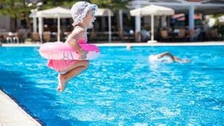 Ein kleines Mädchen mit Schwimmring hüpft in das Becken in einem Schwimmbad.