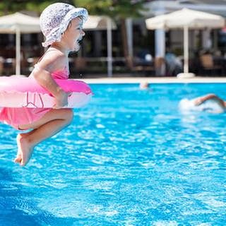 Ein kleines Mädchen mit Schwimmring hüpft in das Becken in einem Schwimmbad.