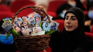 Eine schiitische Frau hält einen Korb voller Porträts von Hisbollah-Kämpfern, die während einer Kundgebung zum Märtyrertag der Hisbollah im südlichen Vorort von Beirut im Libanon im Kampf mit ihrer Gruppe starben