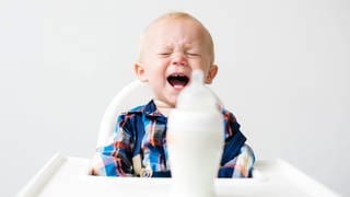 Ein kleiner Junge schreit, vor sich eine Milchflasche: Wie wichtig das Schreien ist, zeigen Babys: Mal schreien sie, um zu kommunizieren, dass sie Hunger oder Schmerzen haben, mal weil sie sich langweilen. Analysen zeigen, dass Babys schreiend ihre Muttersprache einüben. 